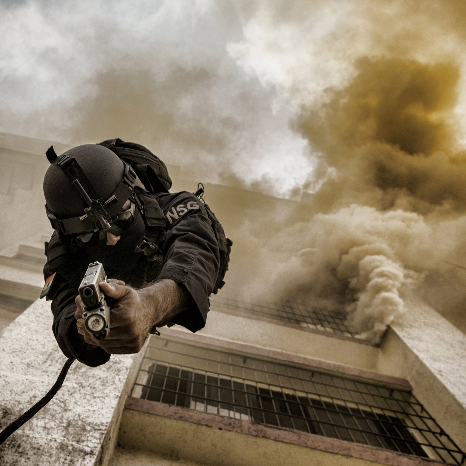 An inverted descent during building-intervention training, with body, weapon and architecture held in one frame.